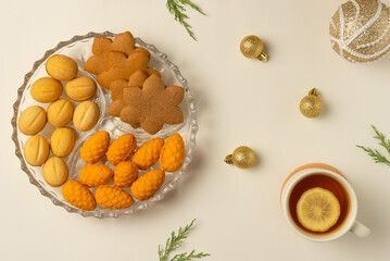 Plate with cookies, cup of tea and Christmas balls on beige background. Flat lay, top view.