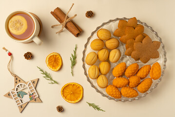 Plate with cookies, cup of tea and Christmas decoration on beige background. Flat lay, top view.