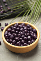 Ripe acai berries in bowl on grey textured table, closeup