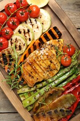 Delicious grilled vegetables and chicken breast on wooden table, top view