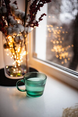 Green glass full of water. A bunch of white cotton flowers with branches with red berries