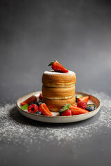 Stack of fluffy Japanese pancakes served with fresh berries and a dusting of powdered sugar on a ceramic plate. Gourmet breakfast, dessert indulgence and elegant food styling in a minimalistic setting