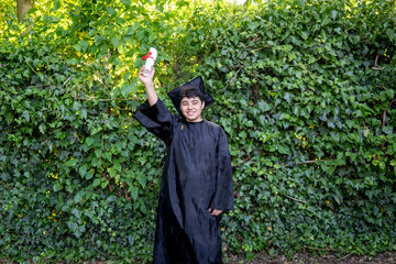 Young recent graduate boy, dressed in cap and gown, showing off his degree, celebrating