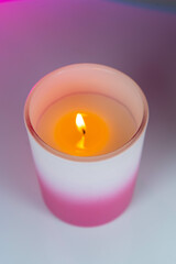 A glowing candle on a table against a pink and purple background.