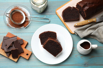 Tasty chocolate sponge cake and ingredients on light blue wooden table, top view