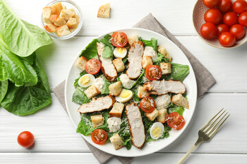 Tasty Caesar salad with chicken and tomatoes on white wooden table, flat lay