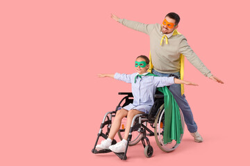 Little girl in wheelchair and her father dressed as superheroes on pink background © Pixel-Shot