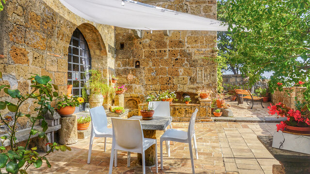 Charming European courtyard in the historic town of Civita di Bagnoregio, Italy, showcasing a beautiful garden, classical architecture, and rustic outdoor furniture, table and chairs