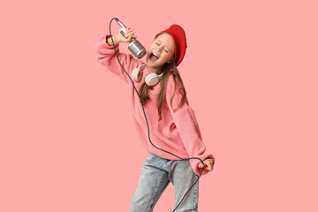 Cute girl singing with modern microphone and headphones on pink background