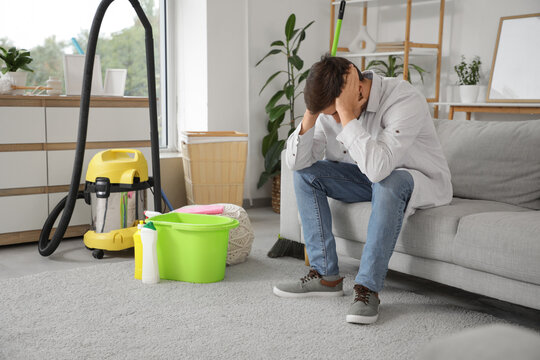 Stressed young man sitting on sofa after cleaning at home - Powered by Adobe