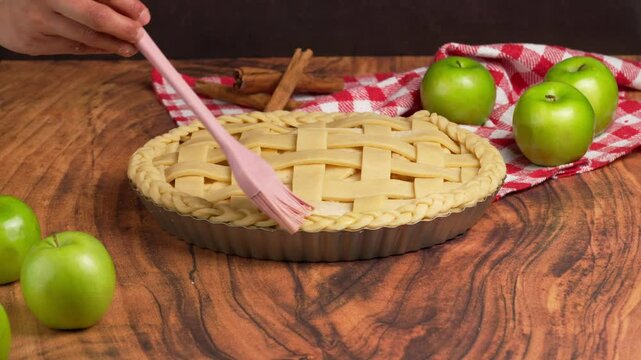Preparing an apple pie, hands of a woman brush the pie crust with an egg wash, green apple, cinnamon, apple tart