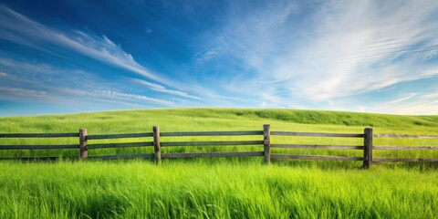 Fototapeta premium Serene pastoral scene of a wooden fence bordering a vibrant green field under a bright blue sky with wispy clouds