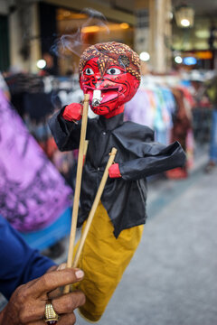 A vendor holding a traditional Cepot puppet, a vibrant character from Sundanese Wayang Golek. Ideal for themes of Indonesian culture, heritage, folk art, and traditional craftsmanship