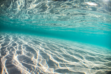Crystal-clear waters with intricate light patterns on the sandy floor, captured underwater at...