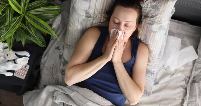 A woman is lying in bed, feeling unwell, sick and surrounded by a lot of tissues, taking care of herself during this difficult time