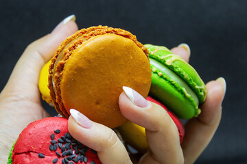 Colorful macarons held in a hand against a dark background