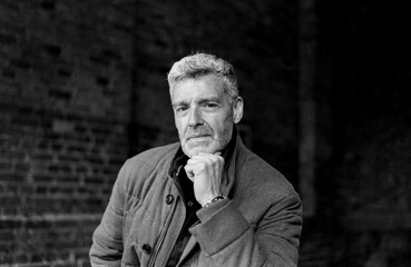Pensive mature man posing with hand on chin in monochrome, grainy film portrait