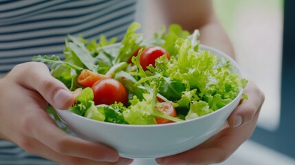 A person holds a bowl of fresh salad, featuring vibrant greens and cherry tomatoes, showcasing healthy eating and vibrant colors.