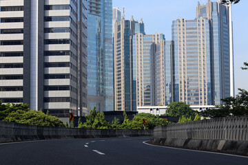 A modern cityscape features sleek skyscrapers against a clear blue sky, with a winding road leading through lush greenery, inviting exploration and adventure.