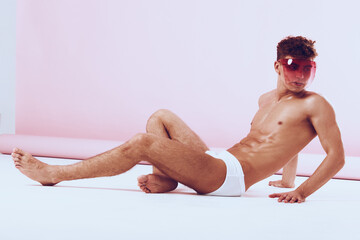 Obraz premium Stylish young man lounging in minimalistic setting, wearing sunglasses and sporty white shorts, showcasing confidence and modern fashion.