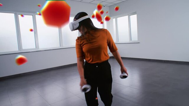 Asian young woman in virtual reality headset paints with wireless controllers, uses gestures to create abstract online artwork. Holographic 3D animation of paint drops. Augmented reality technology.