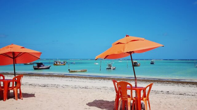 Paradise scene of S&atilde;o Jos&eacute; da Coroa Grande, Pernambuco, Brazil, with turquoise waters, boats in the background, and a colorful beach umbrella enhancing the tropical vibe.