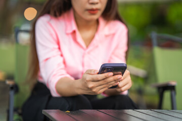 A young woman walks along a grassy path in a green forest, enjoying sunlight and nature. She relaxes, looks at her new mobile phone, and embraces the peaceful outdoor environment