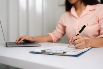 Fototapeta premium A close-up of a businesswoman working on a laptop in an office. As an accountant, she records financial data, verifies documents, manages income and expenses, ensuring accurate financial reporting