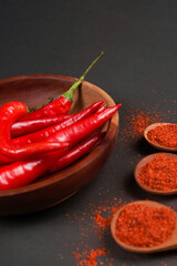 Large red chili and chilli powder served on wooden bowk isolated on a black background