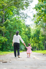 A mother carries her little daughter through a green space surrounded by trees. They enjoy fresh air, outdoor fun, and quality time together, embracing nature on a beautiful sunny day