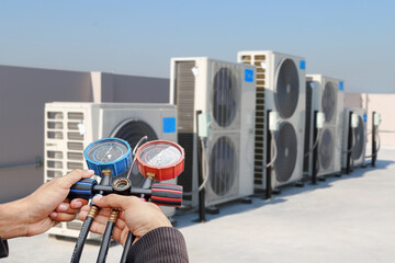Air conditioning, HVAC service technician using gauges to check refrigerant and add refrigerant.