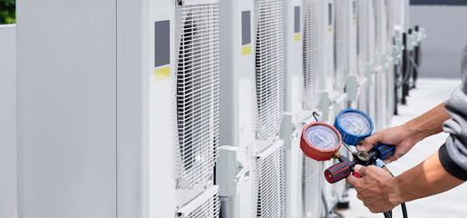 Air conditioning, HVAC service technician using gauges to check refrigerant and add refrigerant.	