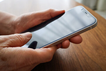 テーブルでスマホを操作するシニア女性の手元