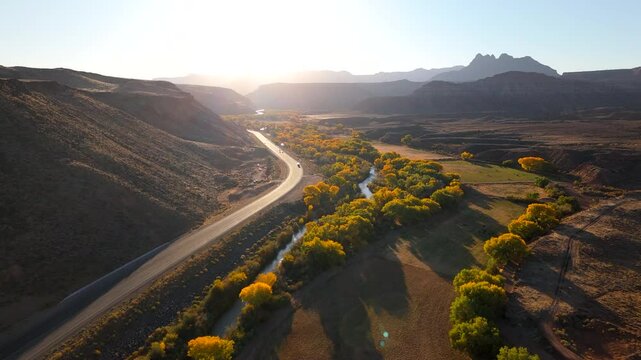 This breathtaking aerial shot captures the mesmerizing beauty of Zion National Park, showcasing vibrant fall foliage and impressive rock formations bathed in the stunning light of sunset in Utah