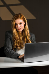 A young woman with red hair works at a laptop. A female student studies at a laptop. The concept of remote work. Portrait of an office worker