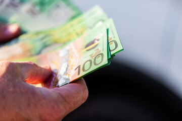 Middle aged mans hand holding one hundred dollar notes in Australian cash to pay for car