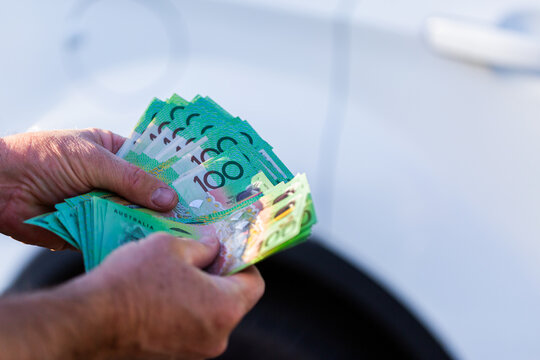 Middle aged mans hand holding one hundred dollar notes in Australian cash to pay for car