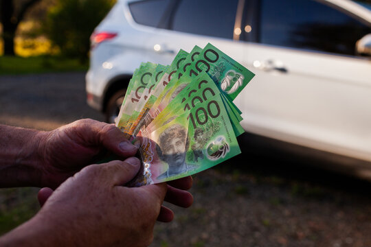 Middle aged mans hand holding one hundred dollar notes in Australian cash to pay for car