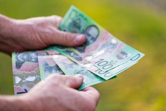 Middle aged man&rsquo;s hand holding hundreds of dollars of Australian cash