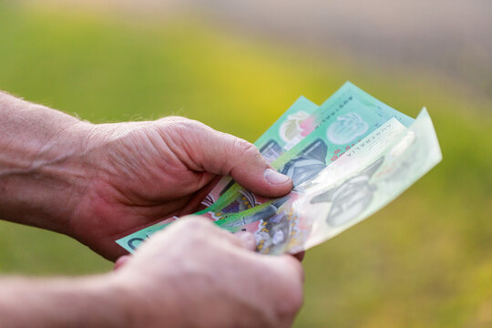 Middle aged man&rsquo;s hand holding hundreds of dollars of Australian cash