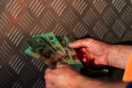 Middle aged man&rsquo;s hand holding hundreds of dollars of Australian cash beside meal texture