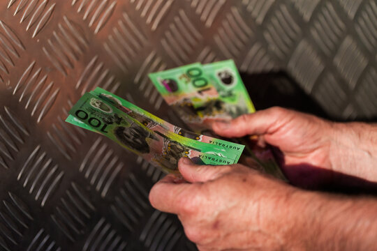 Middle aged man&rsquo;s hand holding hundreds of dollars of Australian cash beside meal texture