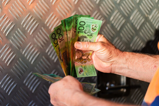Middle aged man holding hundreds of dollars of Australian cash beside meal tool box on ute