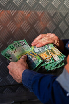 Middle aged man holding hundreds of dollars of Australian cash beside meal toolbox on ute