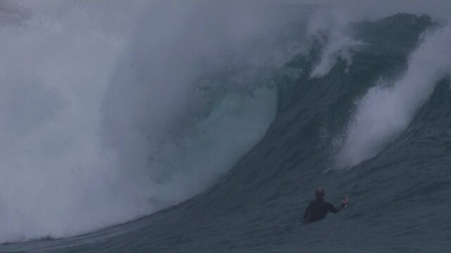 Surfers wait in lineup as a powerful wave barrels, foam ball spitting out in slow motion