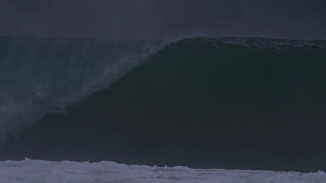 Massive wave crashes forward, creating a barrel with mist streaming off in dark tones