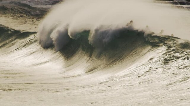 Slow motion shot of surfers in lineup as large waves barrel, mist blowing off at dawn