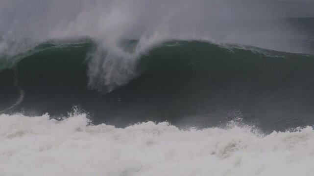 Large wave barrels forward, mist blowing from the crest in dramatic, dark blue light
