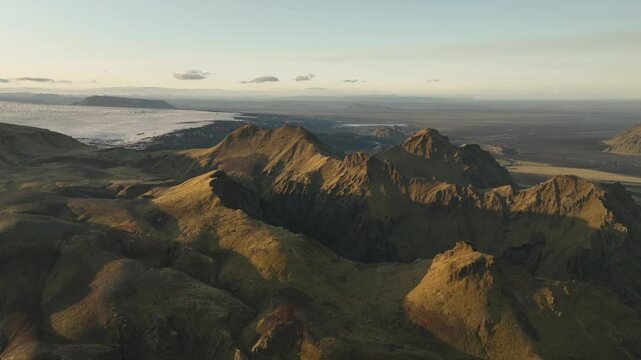 An aerial view of Thakgil, Iceland, showcasing golden volcanic peaks, distant glaciers, and sprawling plains under a serene sky.
