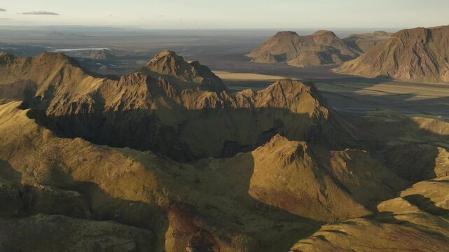 A striking aerial view of Thakgil, Iceland, showcasing golden-hued volcanic peaks casting deep shadows across the expansive rugged landscape.